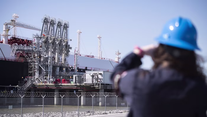 A person wearing a blue hard hat observes an LNG tanker docked at the Cheniere Sabine Pass Liquefaction facility