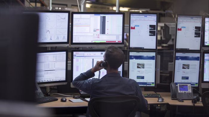 A financial trader speaks on a telephone while monitoring multiple data and trading screens on the Amsterdam Stock Exchange trading floor.