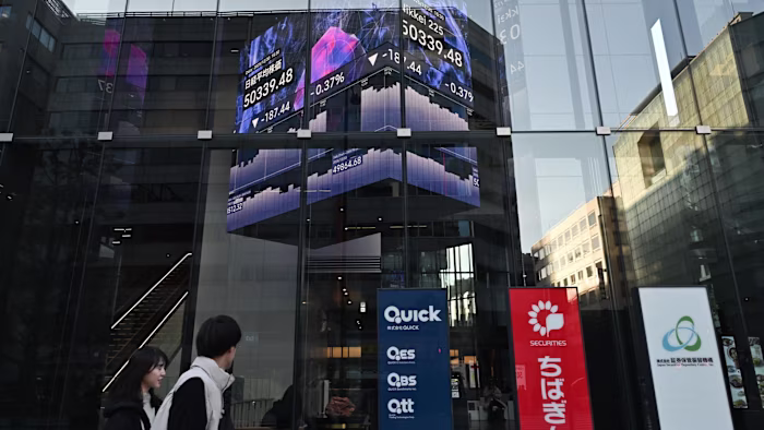 People walk by a stock market indicator board on the final trading day of the year in Tokyo on Tuesday