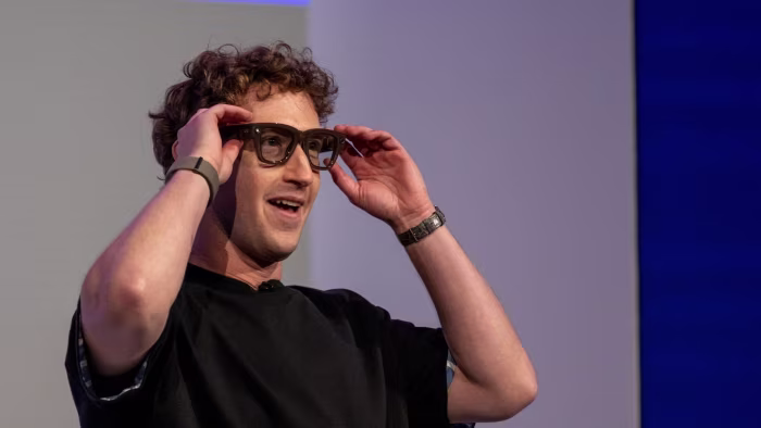 Mark Zuckerberg puts on Meta Ray-Ban Display AI glasses, smiling, during a presentation at the Meta Connect event.