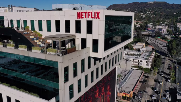 Netflix logo atop Sunset Bronson Studios office building with the Hollywood sign visible in the distant hills.