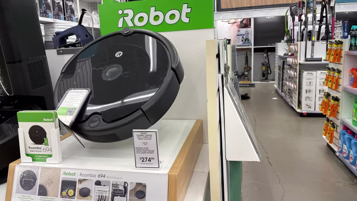 Roomba 694 robot vacuum displayed on a shelf in a Bed Bath and Beyond store with iRobot branding and a price tag.