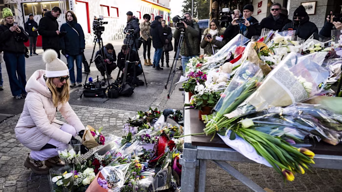 People gather near a memorial of flowers and tributes to honor victims of the Le Constellation bar fire in Crans-Montana.