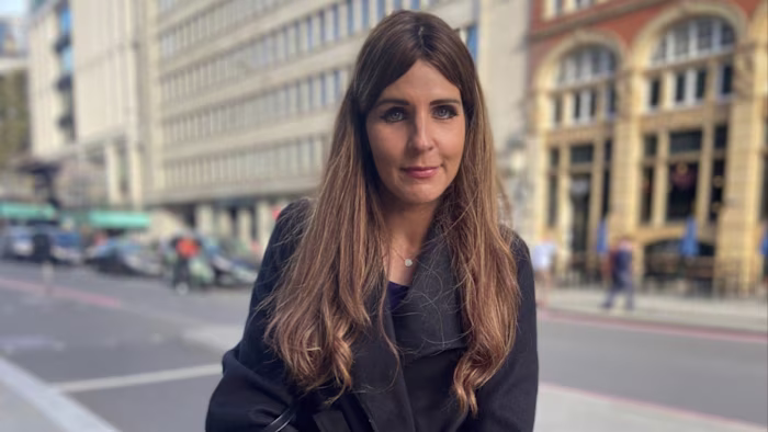 Gabby Stonkute stands on a City street, looking at the camera, with buildings and cars in the background.