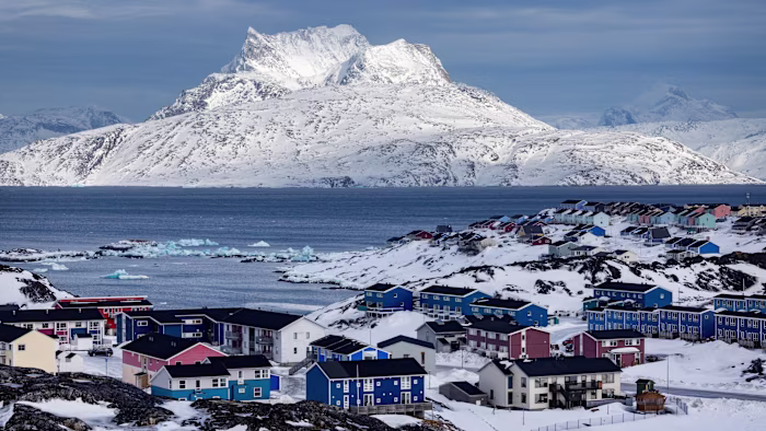 Colorful houses of Nuuk are scattered across snowy hills, with icebergs in the water and the snow-covered Sermitsiaq mountain in the background.