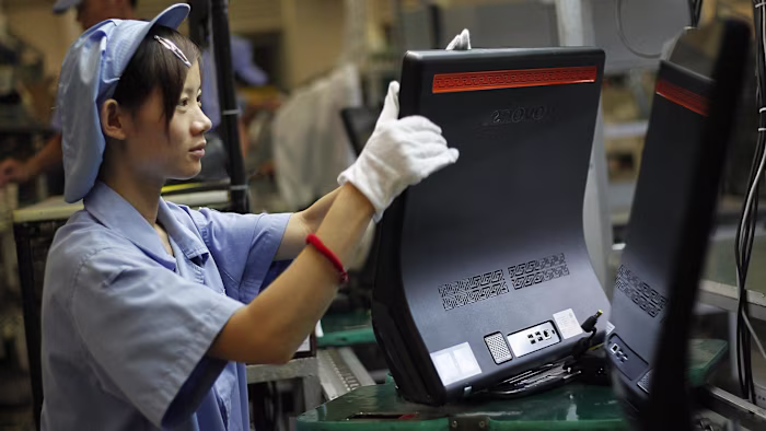 A worker in a blue uniform and cap assembles Lenovo computers on a production line at a factory.