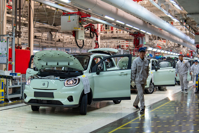 Lavoratori in uniforme assemblano veicoli elettrici bianchi su una linea di fabbrica automatizzata nella fabbrica intelligente di Leapmotor.