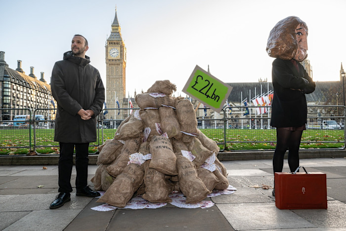 Zak Polanski sta accanto a una pila di sacchi etichettati come 