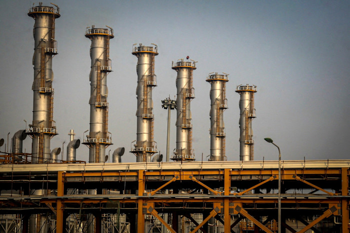 Alte torri di metallo in una raffineria di gas naturale con fiamme visibili che si innalzano da uno dei cumuli.